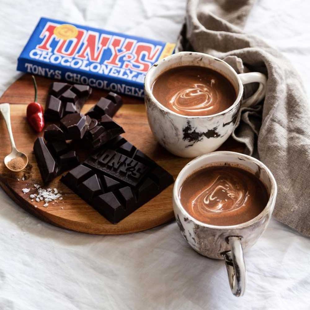 Tony's Chocolonely dark chocolate in blue packet in living space with hot chocolates and assorted ingredients